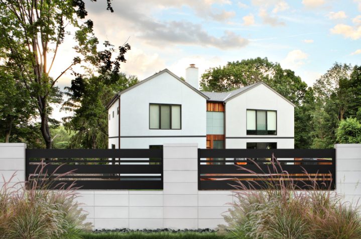 betonowe ogrodzenie firmy JONIEC® z czarnymi poziomymi panelami i eleganckim domem w tle, otoczone zielenią